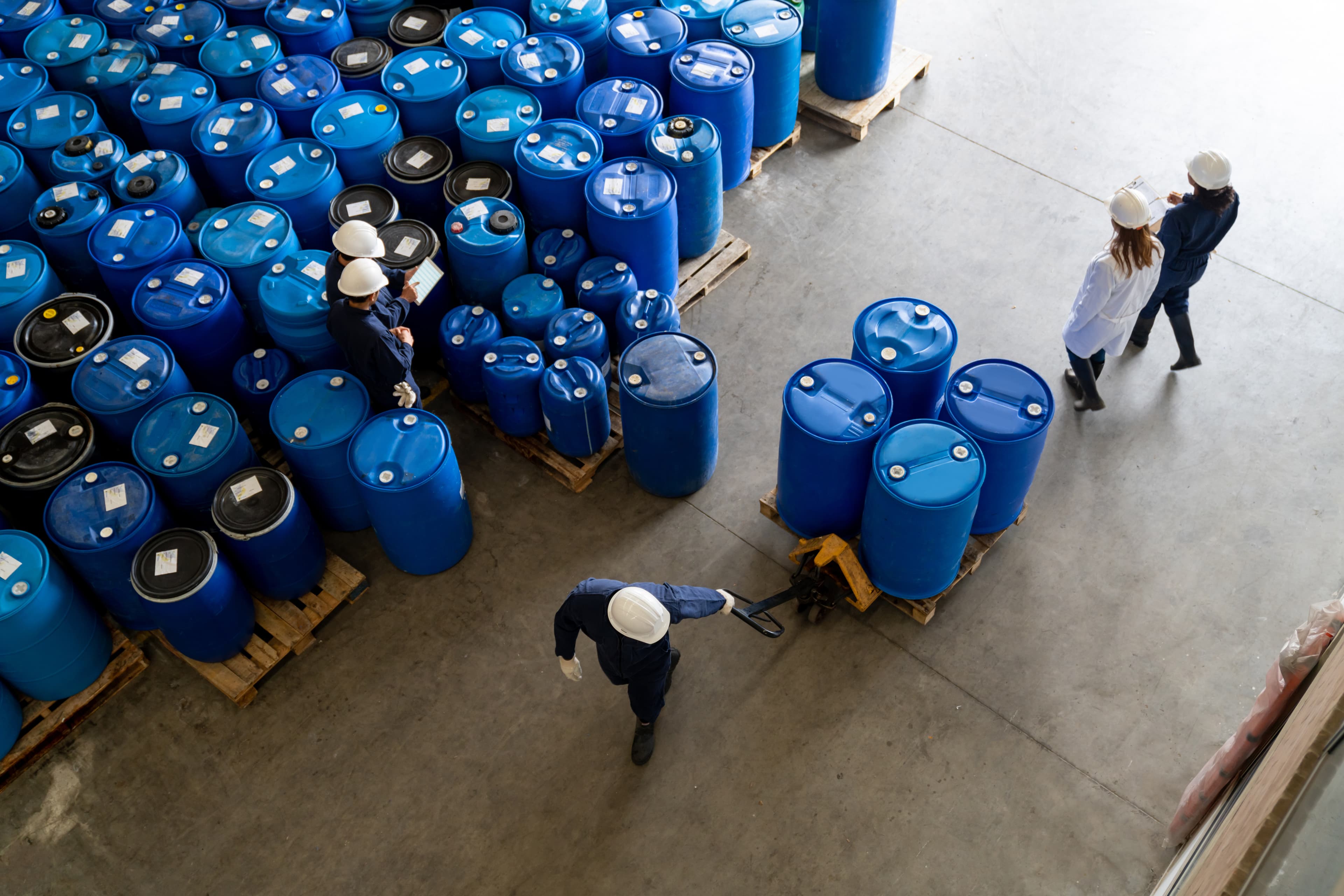 Team of Latin American employees working at a chemical plant moving barrels of substances at a warehouse - industrial concepts